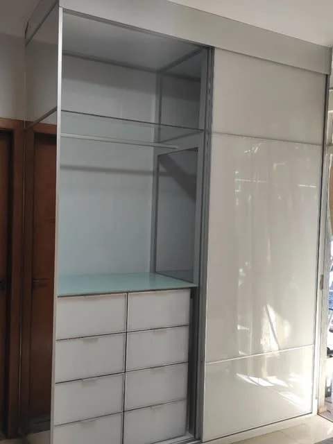 Closet com portas de correr em vidro branco e gavetas com frente de vidro e perfis de alumínio