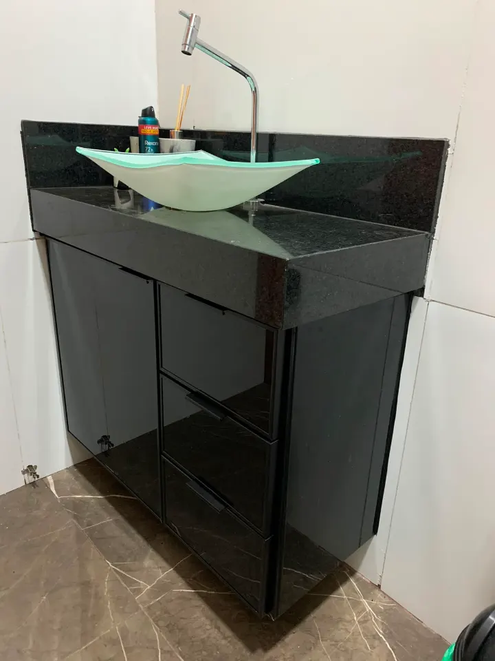 Bancada de banheiro com cuba de vidro e armário de vidro preto sob o granito