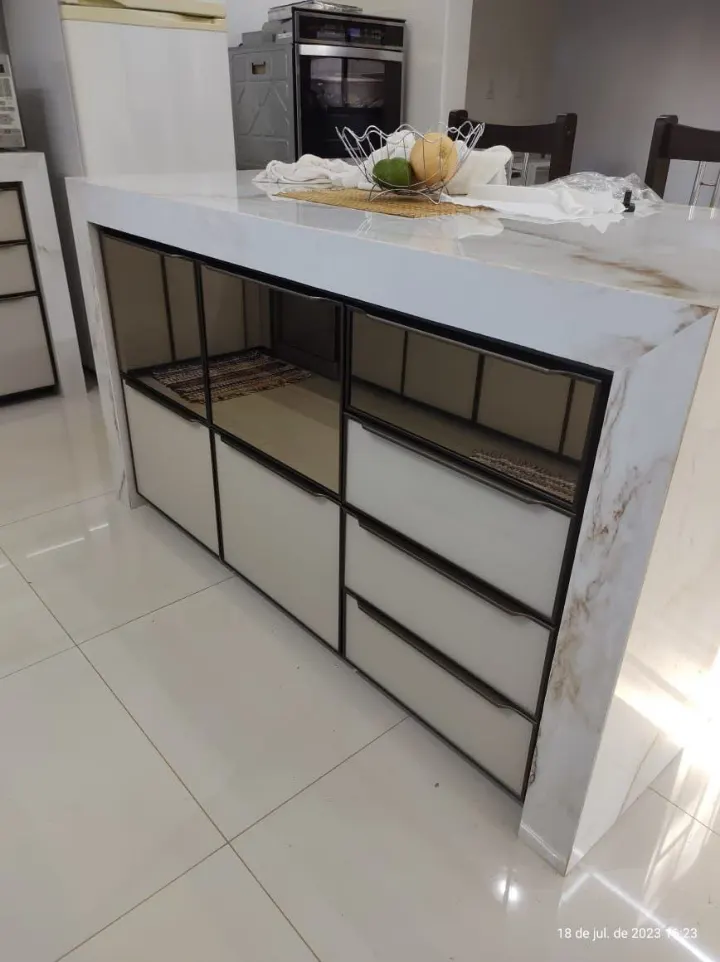 Ilha de cozinha com tampo de porcelanato e portas e gavetas em vidro espelhado com perfis pretos
