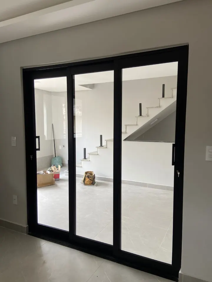 Porta de correr de três folhas em alumínio preto e vidro, com escada ao fundo
