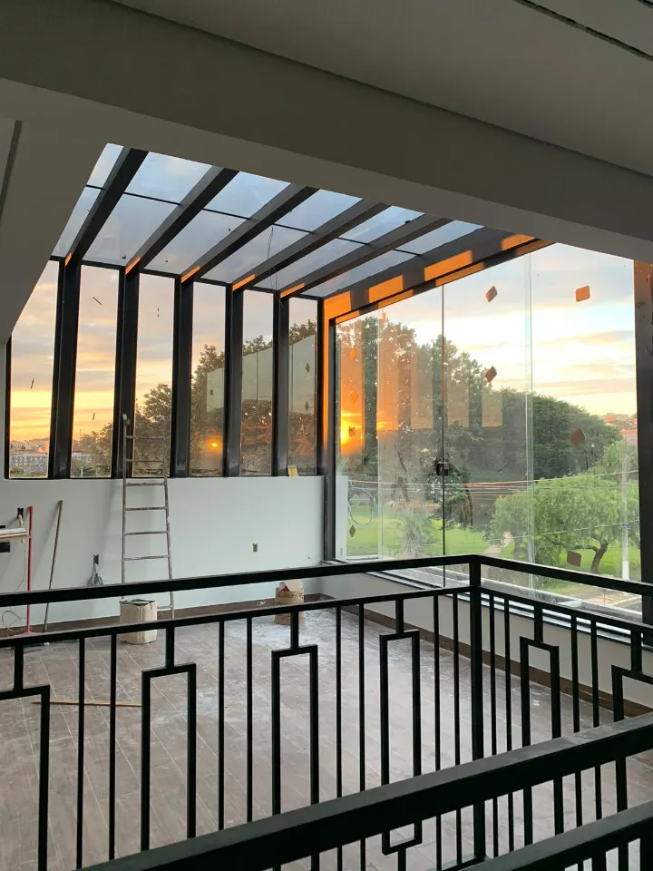 Varanda com cobertura de vidro, fechamento lateral de vidro e guarda-corpo de ferro ao pôr do sol